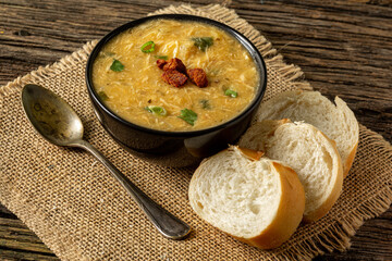 Caldo de Kenga Cassava broth with shredded chicken, typical Brazilian food known as (Caldo de Quenga), in a black pot on top of a rustica with a spoon and slices of bread, with selective focus