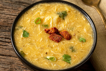Caldo de Kenga Cassava broth with shredded chicken, typical Brazilian food known as (Caldo de Quenga), in a black pot on top of a rustica with a spoon and slices of bread,  with selective focus