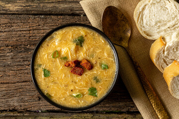 Caldo de Kenga Cassava broth with shredded chicken, typical Brazilian food known as (Caldo de Quenga), in a black pot on top of a rustica with a spoon and slices of bread,  with selective focus