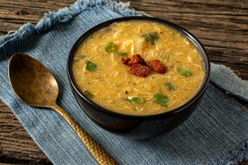 Caldo de Kenga Cassava broth with shredded chicken, typical Brazilian food known as (Caldo de Quenga), in a black pot on top of a rustica with a spoon and slices of bread,  with selective focus