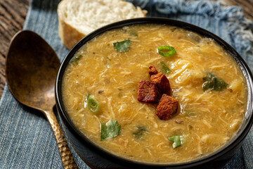Caldo de Kenga Cassava broth with shredded chicken, typical Brazilian food known as (Caldo de Quenga), in a black pot on top of a rustica with a spoon and slices of bread,  with selective focus