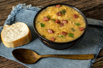 Caldo de Kenga Cassava broth with shredded chicken, typical Brazilian food known as (Caldo de Quenga), in a black pot on top of a rustica with a spoon and slices of bread,  with selective focus