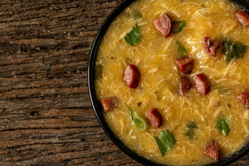 Caldo de Kenga Cassava broth with shredded chicken, typical Brazilian food known as (Caldo de Quenga), in a black pot on top of a rustica with a spoon and slices of bread,  with selective focus