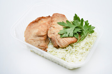 Juicy fried chicken pieces with a side dish of rice. Delicious breakfast in a plastic container.