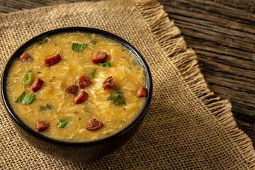 Caldo de Kenga Cassava broth with shredded chicken, typical Brazilian food known as (Caldo de Quenga), in a black pot on top of a rustica with a spoon and slices of bread,  with selective focus