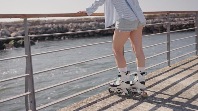 Woman in casual attire rollerblading by the waterfront, enjoying a sunny day near the sea. Wearing shorts and striped shirt.
