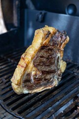 Close up shot of a big, fat, juicy t-bone steak cooking on the barbecue grill, releasing juices from the fat and looking mouth watering and delicious.