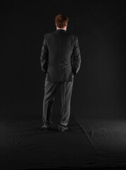 Fototapeta premium MAN businessman IN A SUIT stands with his back on a black background