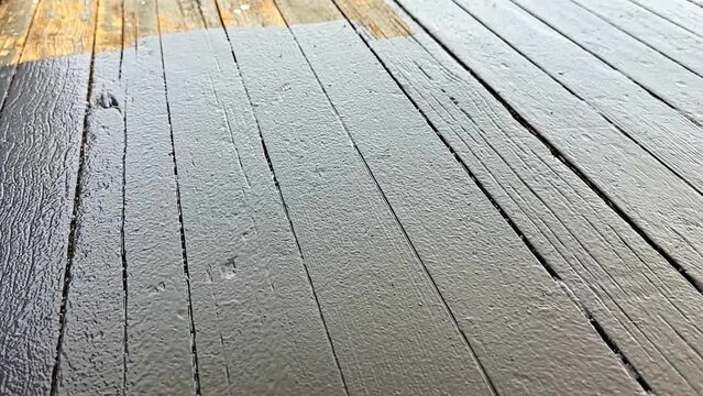 A close-up shot of a paint roller being used to paint a wooden deck with dark gray color