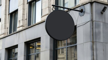 A black circle sign on the side of an urban building, serving as a mockup template with blank space for text or logo, positioned as a black round wall hanging billboard in a city street.
