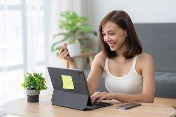 Young woman working from home with a laptop, enjoying a cup of coffee. Modern workspace setup with a relaxed and productive atmosphere.