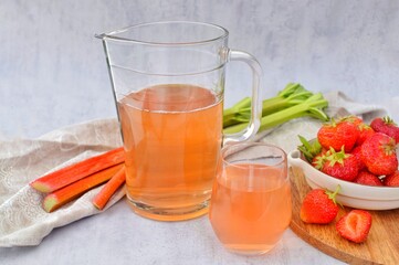 Compote of fresh strawberries and rhubarb with mint leaves in a glass and jug.