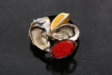 Plate of tasty oysters with lemon and red caviar on black background