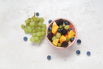 Bowl of fresh fruit salad with grapes and blueberry on light background