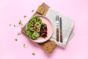 Plate of fresh vegetable salad with beet and bread on pink background