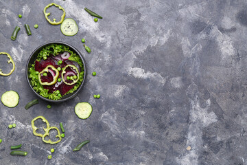 Bowl of fresh vegetable salad with beet and ingredients on grey background