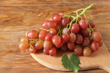 Board with tasty ripe grapes on wooden background