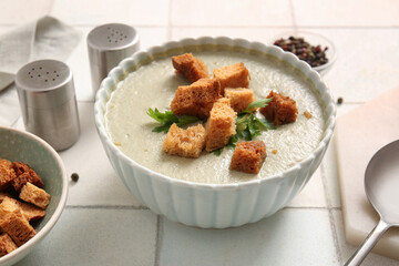 Bowl of tasty cream soup with croutons on white tile background