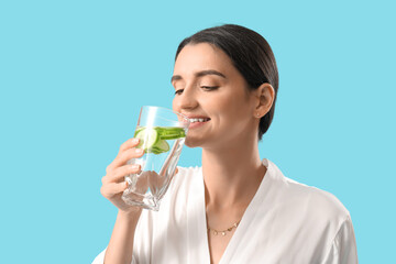 Young woman drinking cucumber water on blue background