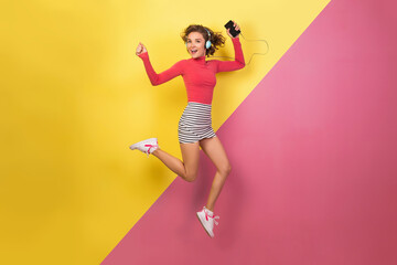 smiling attractive smiling excited woman in stylish colorful outfit jumping and listening to music