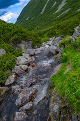 A landscape of a small waterfall flanked by large rocks against a backdrop of green mountains