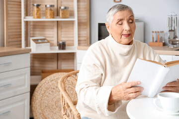 Senior woman reading book at table in kitchen