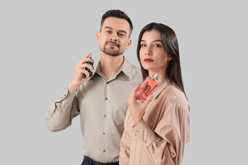 Young couple with bottles of perfume on light background