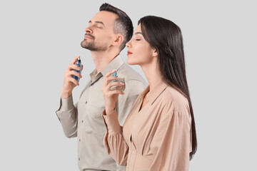 Young couple applying perfume on light background