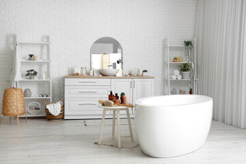 Table with skin care products near white bathtub in light bathroom