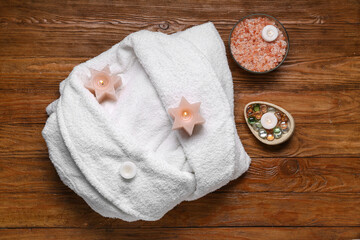 White soft bathrobe with sea salt and burning candles on wooden background