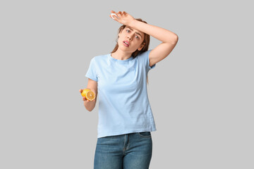 Young woman with lemon and nasal spray suffering from allergy on grey background
