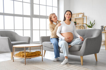 Obraz premium Young pregnant woman with doula sitting on sofa at home