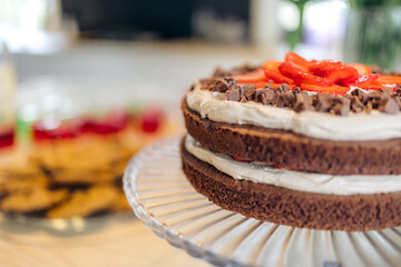 A close-up of a chocolate cake with strawberries on top standing on a glass tray