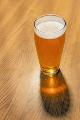 A glass of yellow beer with a cast shadow on the table