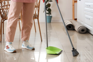 Woman sweeping tile floor with broom and dustpan at home