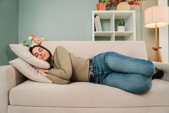 Full leght view of a female napping at living room couch, having a good dream with positive expression. Sleeping young adult woman taking nap on the sofa during the day. Paceful lady taking a siesta