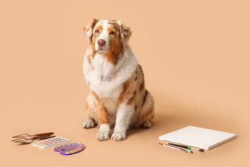 Cute dog with artist's supplies on beige background