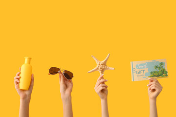 Female hands with sunscreen, sunglasses, starfish and travel gift voucher on yellow background....