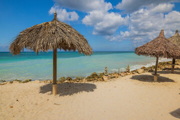 Beautiful view of the Caribbean Sea's blue waters and sandy beach with palm leaf sun umbrellas on Aruba.