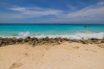 Beautiful view of waves from the Caribbean Sea rolling onto a sandy beach protected by stones. Aruba.