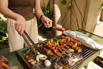 Hands of woman cooking food on grill in backyard