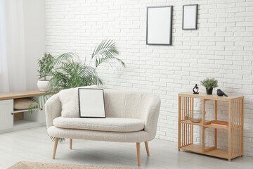 Fototapeta premium Modern living room with houseplant and blank picture frame on sofa and white brick wall