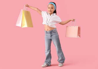 Fototapeta premium Portrait of fashionable little girl with shopping bags on pink background