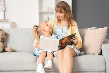 Nanny reading story to little girl on sofa at home