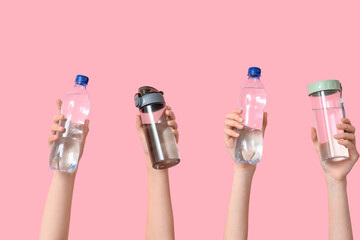 Female hands with different bottles of water on pink background, closeup