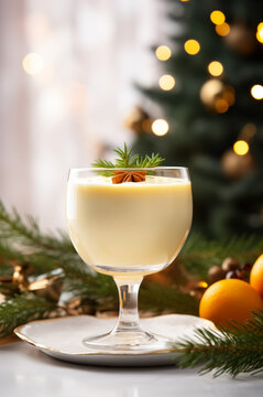 Festive Christmas eggnog in a glass, garnished with star anise and evergreen sprigs, with a blurry Christmas tree and warm lighting in the background.

