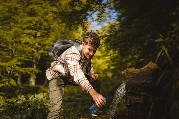 Adult young caucasian man pour water at the spring in the forest