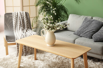 Sofa, houseplant and vase with beautiful blooming branches on table in interior of stylish living room