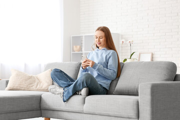 Young woman chatting with mobile phone on sofa in stylish living room