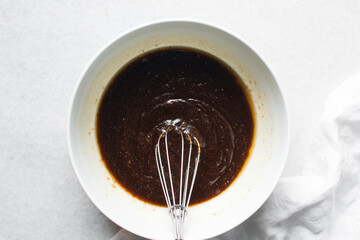 overhead view of melted butter white sugar and brown sugar cocoa powder in a white bowl, the process of making brownies, mixing butter and sugar to make brownies